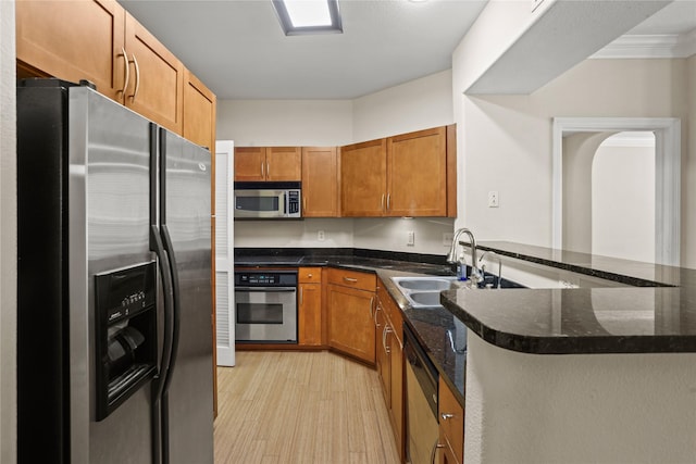 kitchen with sink, dark stone counters, kitchen peninsula, stainless steel appliances, and light hardwood / wood-style flooring