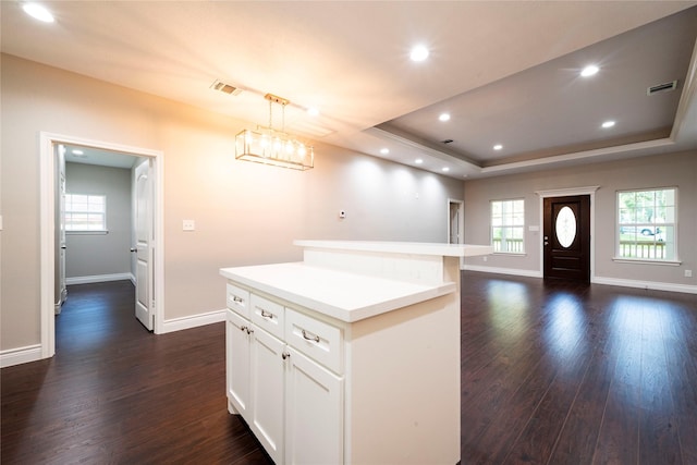 kitchen with a kitchen island, dark hardwood / wood-style floors, decorative light fixtures, white cabinetry, and a tray ceiling