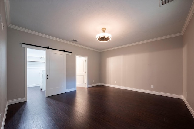 empty room with dark wood-type flooring, ornamental molding, and a barn door