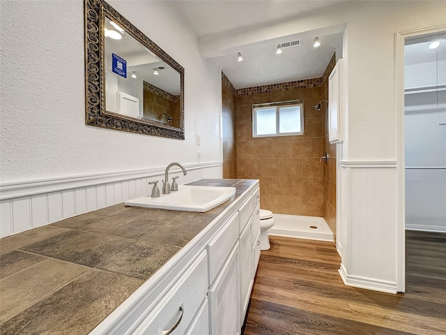 bathroom with hardwood / wood-style flooring, vanity, toilet, and a tile shower