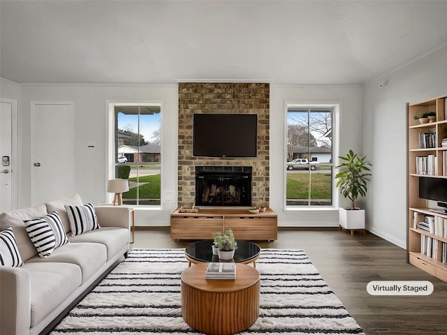 living room with dark wood-type flooring, ornamental molding, and a brick fireplace