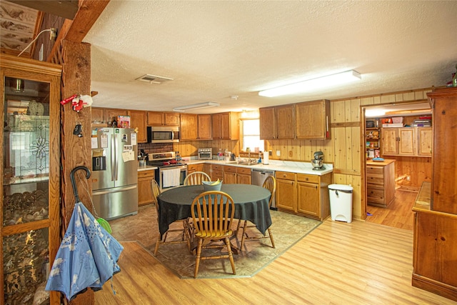 kitchen with appliances with stainless steel finishes, sink, wooden walls, and light hardwood / wood-style flooring