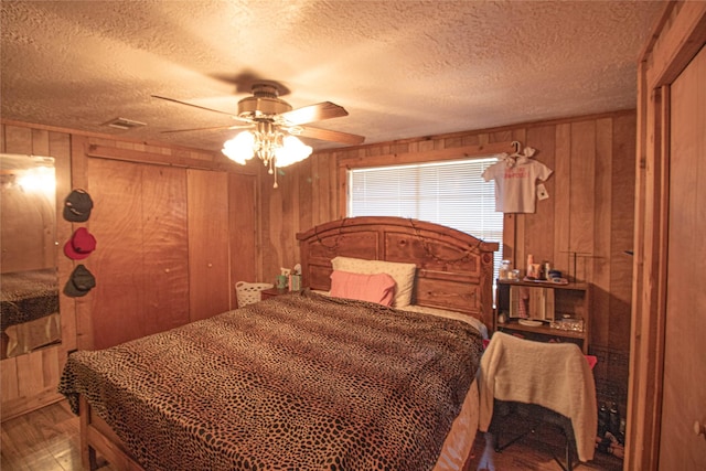 bedroom featuring ceiling fan, wood-type flooring, a textured ceiling, and wood walls