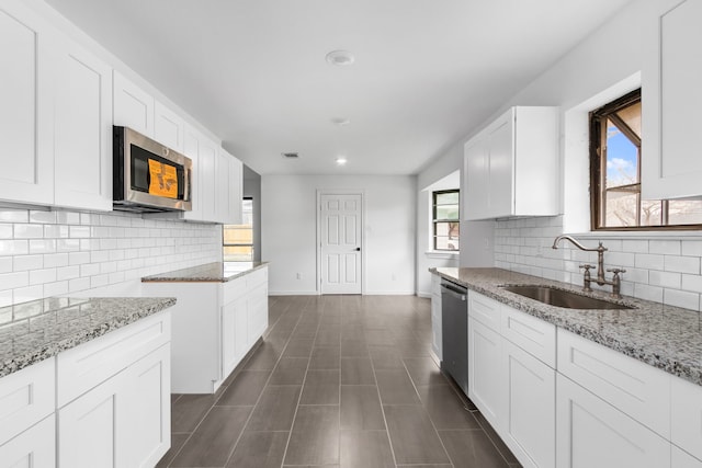 kitchen with appliances with stainless steel finishes, tasteful backsplash, sink, white cabinets, and light stone countertops