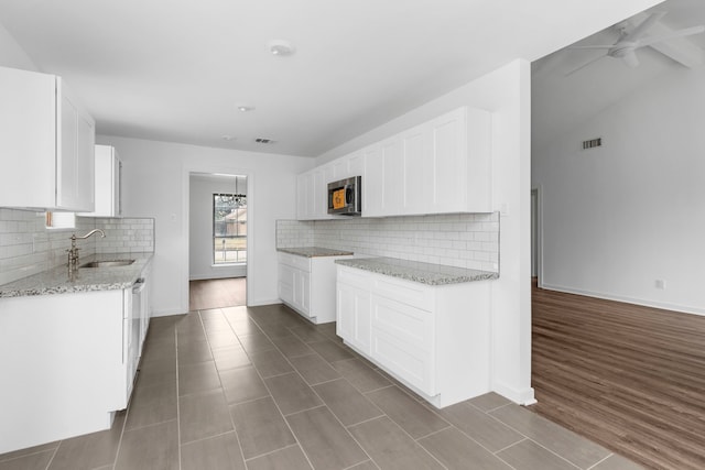 kitchen featuring sink, white cabinets, ceiling fan, light stone countertops, and backsplash