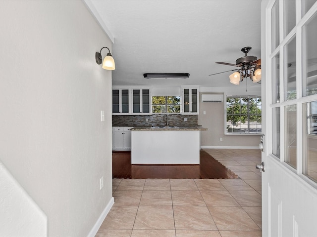 kitchen with an AC wall unit, light tile patterned flooring, backsplash, sink, and white cabinetry