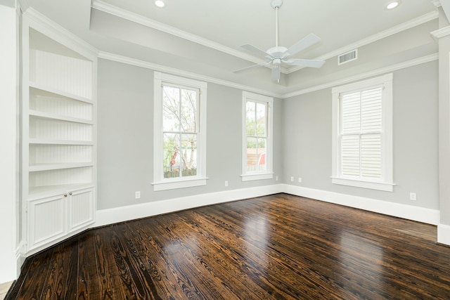 spare room featuring dark hardwood / wood-style floors, ornamental molding, built in features, and a raised ceiling