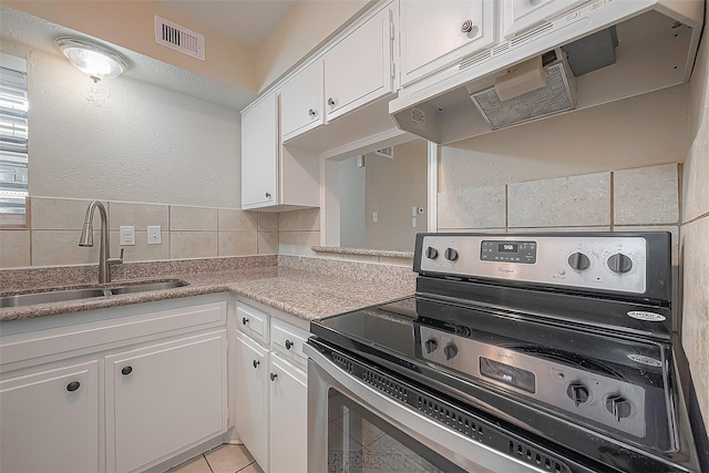 kitchen with light tile patterned flooring, tasteful backsplash, sink, stainless steel range with electric cooktop, and white cabinets