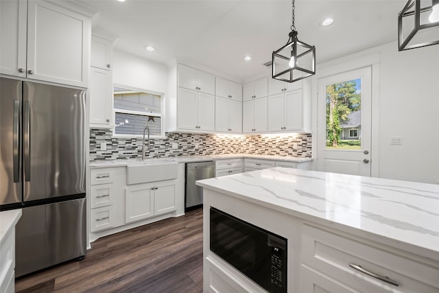 kitchen with appliances with stainless steel finishes, white cabinetry, sink, backsplash, and hanging light fixtures