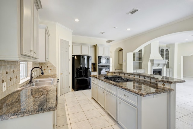 kitchen with light tile patterned flooring, sink, dark stone countertops, a kitchen island, and black appliances