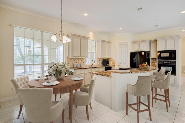 kitchen featuring sink, light stone counters, decorative light fixtures, a kitchen island, and black appliances