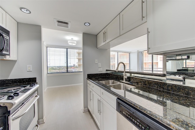 kitchen featuring sink, white cabinetry, light hardwood / wood-style flooring, dark stone countertops, and appliances with stainless steel finishes