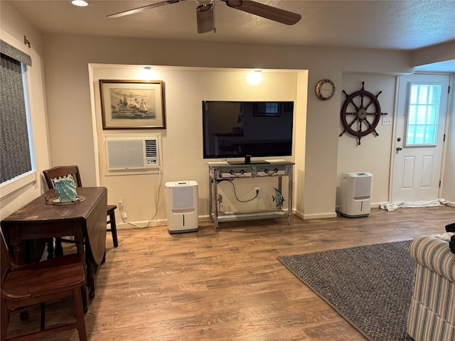 living room with hardwood / wood-style flooring, an AC wall unit, a textured ceiling, and ceiling fan