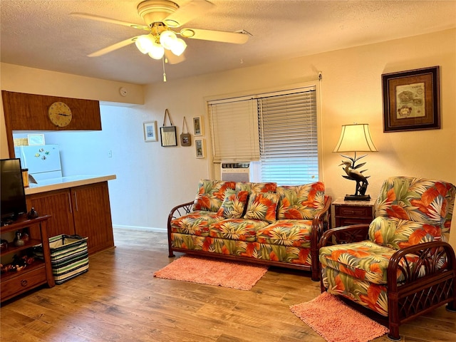 living room featuring ceiling fan, light hardwood / wood-style flooring, and a textured ceiling