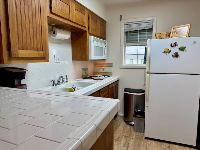 kitchen with sink, tile countertops, white appliances, light hardwood / wood-style floors, and decorative backsplash