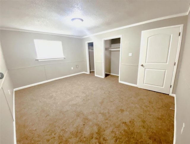 unfurnished bedroom featuring baseboards, crown molding, a textured ceiling, carpet flooring, and two closets