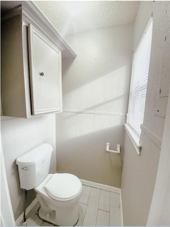 bathroom with a textured ceiling, toilet, and baseboards