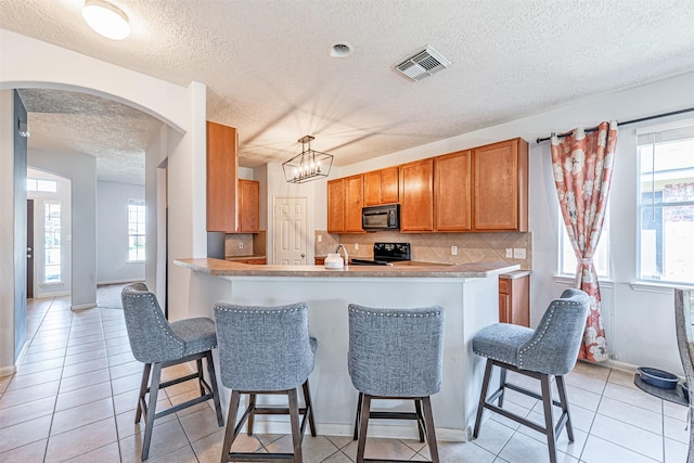 kitchen with a breakfast bar, tasteful backsplash, light tile patterned floors, kitchen peninsula, and black appliances