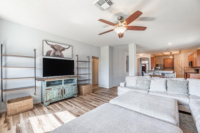 living room featuring ceiling fan, light hardwood / wood-style floors, and a textured ceiling