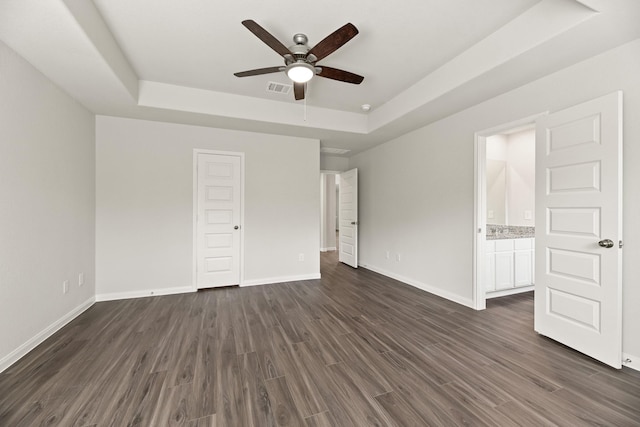 unfurnished bedroom featuring dark wood-style flooring, a raised ceiling, visible vents, and baseboards