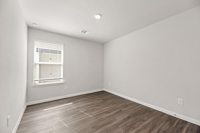 empty room featuring visible vents, baseboards, and dark wood-style flooring