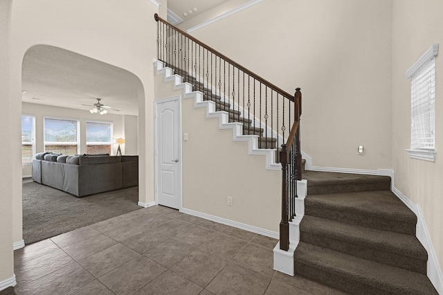 stairway with ceiling fan, carpet flooring, and a high ceiling