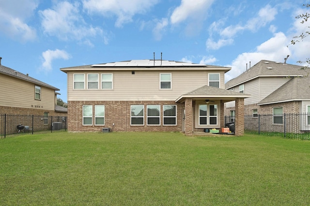 rear view of property featuring a lawn, ceiling fan, and solar panels