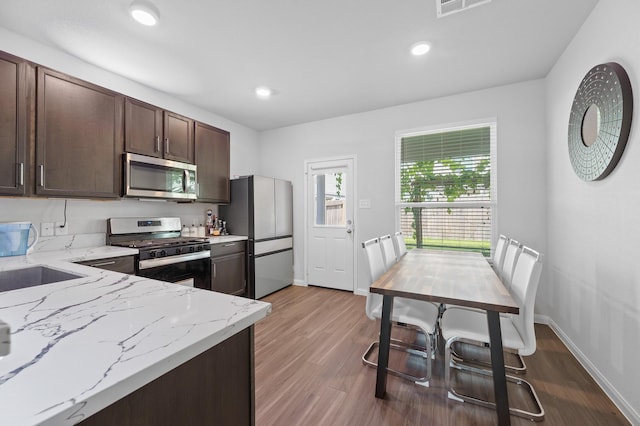 kitchen featuring dark brown cabinetry, sink, light stone counters, appliances with stainless steel finishes, and light hardwood / wood-style floors