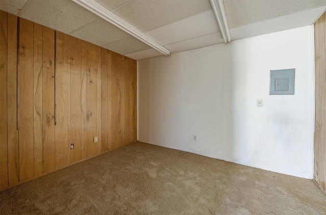 carpeted empty room with a paneled ceiling, electric panel, and wooden walls