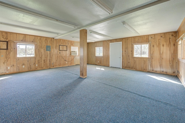 interior space featuring a wall mounted air conditioner, carpet flooring, a textured ceiling, and wood walls