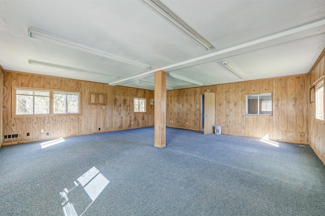 basement featuring a healthy amount of sunlight, dark carpet, and wood walls