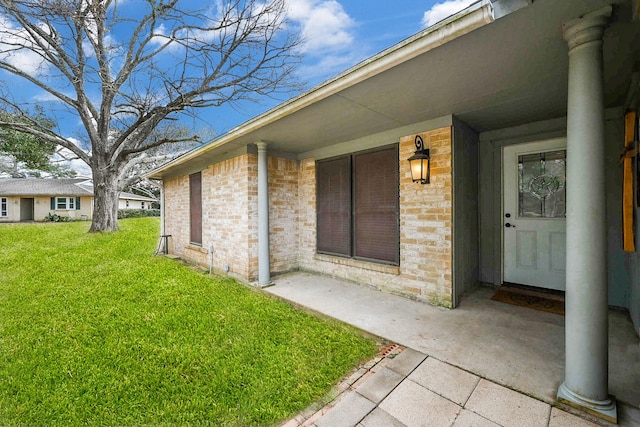 view of exterior entry with a yard and brick siding