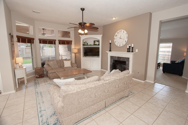 tiled living room featuring ceiling fan, a tiled fireplace, and a wealth of natural light