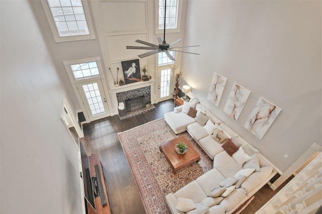 living room featuring ceiling fan, a high end fireplace, dark hardwood / wood-style flooring, and a high ceiling