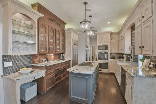 kitchen with hanging light fixtures, light stone countertops, a kitchen island, and built in appliances