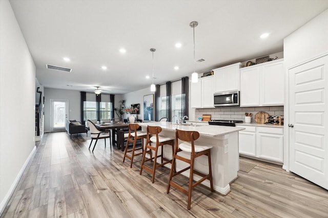 kitchen featuring a breakfast bar, white cabinetry, tasteful backsplash, a center island with sink, and decorative light fixtures