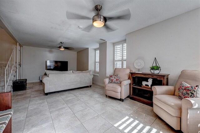 living area with light tile patterned floors, visible vents, stairway, a ceiling fan, and baseboards