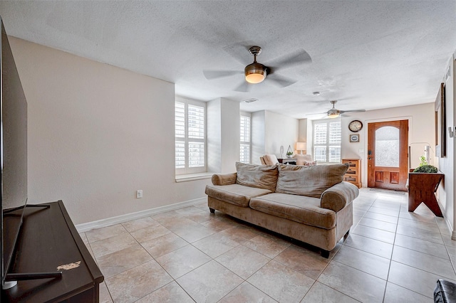 living area featuring light tile patterned floors, visible vents, ceiling fan, a textured ceiling, and baseboards