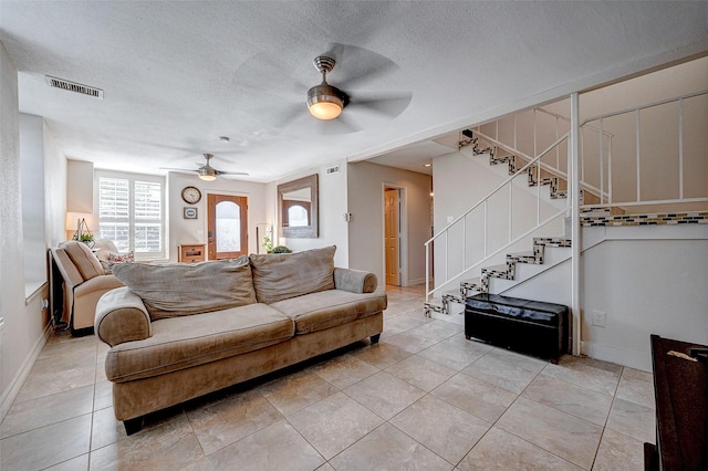 living room with light tile patterned floors, baseboards, ceiling fan, stairway, and a textured ceiling