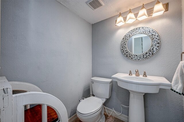 bathroom with toilet, a textured wall, a textured ceiling, and visible vents