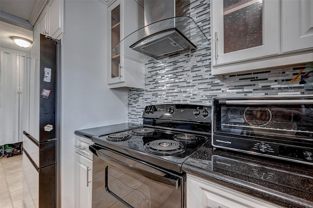 kitchen featuring decorative backsplash, glass insert cabinets, wall chimney range hood, black appliances, and white cabinetry