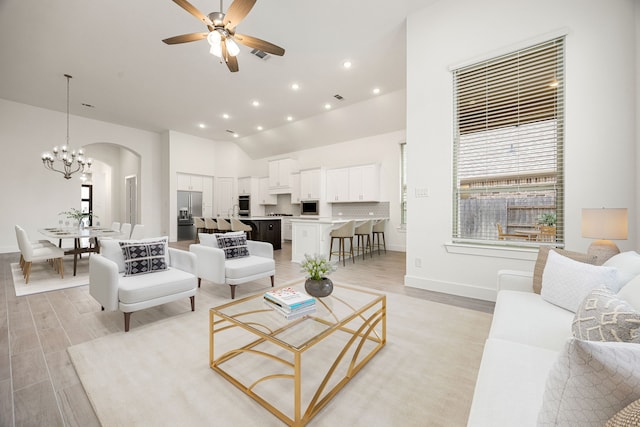 living room featuring ceiling fan with notable chandelier, light hardwood / wood-style flooring, and a high ceiling