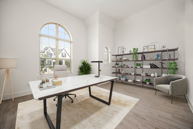 office area with hardwood / wood-style floors, a towering ceiling, and a healthy amount of sunlight