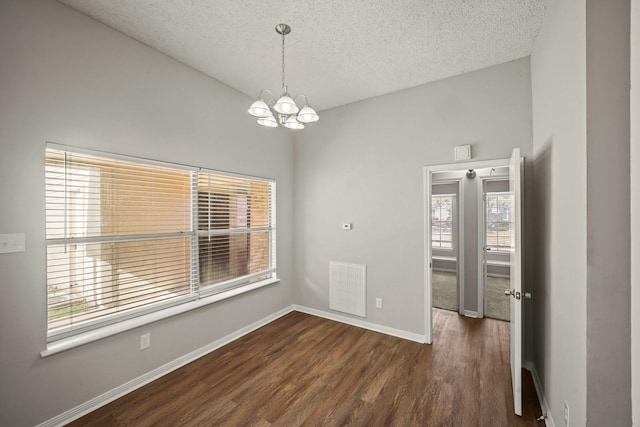 unfurnished room featuring a textured ceiling, a chandelier, visible vents, baseboards, and dark wood finished floors