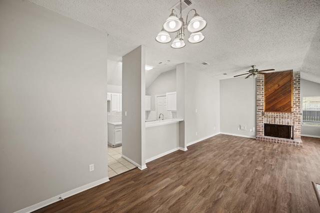 unfurnished living room featuring ceiling fan with notable chandelier, lofted ceiling, a fireplace, and wood finished floors