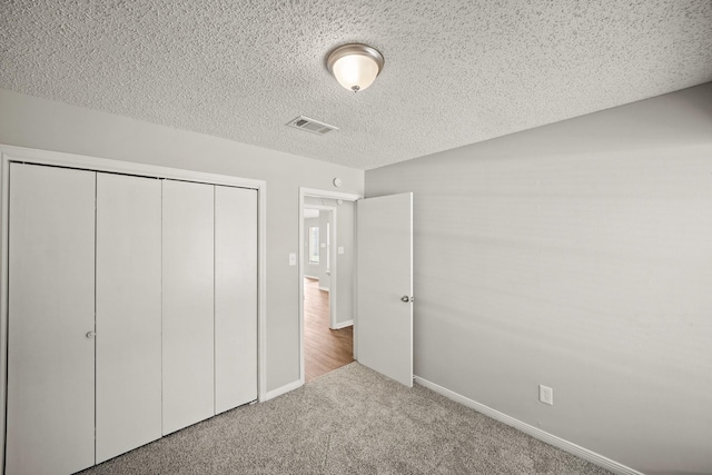 unfurnished bedroom with a textured ceiling, carpet flooring, visible vents, baseboards, and a closet