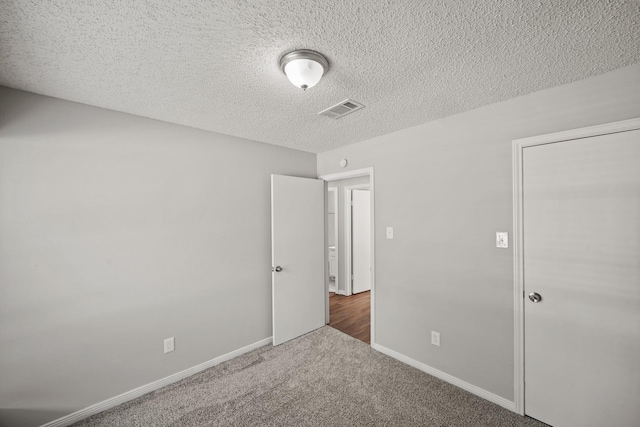 unfurnished bedroom with a textured ceiling, carpet floors, visible vents, and baseboards