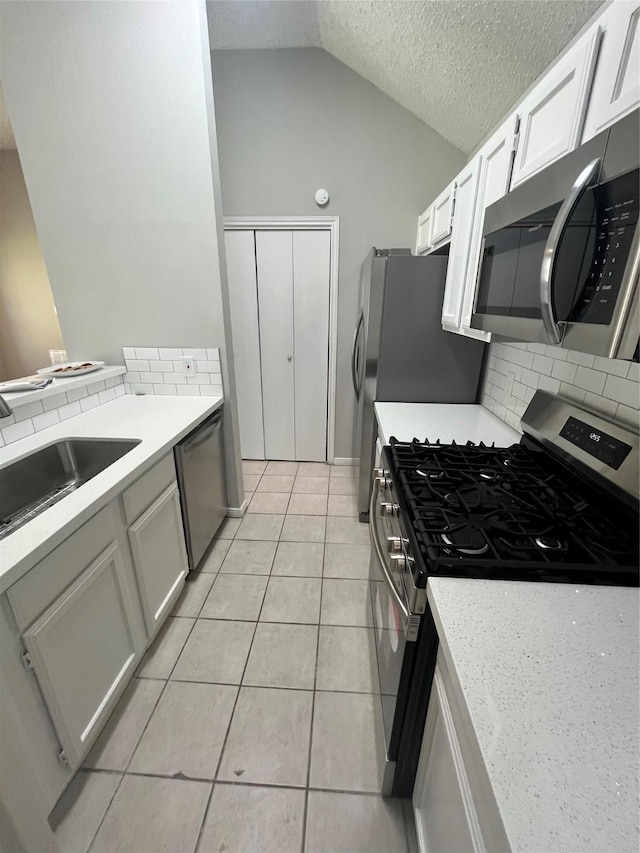 kitchen featuring light tile patterned floors, a sink, vaulted ceiling, light countertops, and appliances with stainless steel finishes