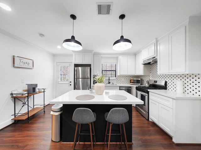 kitchen with under cabinet range hood, stainless steel appliances, dark wood-style flooring, visible vents, and tasteful backsplash