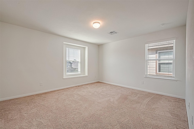 empty room featuring light carpet, visible vents, and baseboards